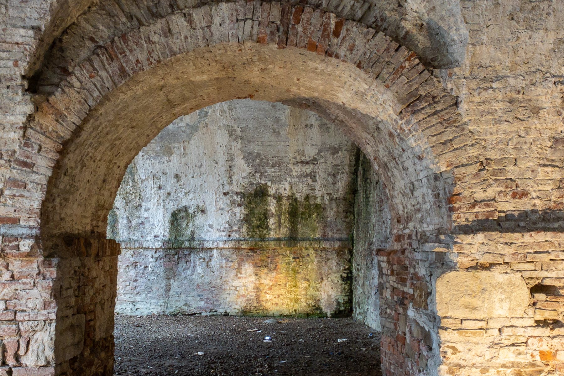 A thick stone archway in an old wall, its opening leading toward daylight.
