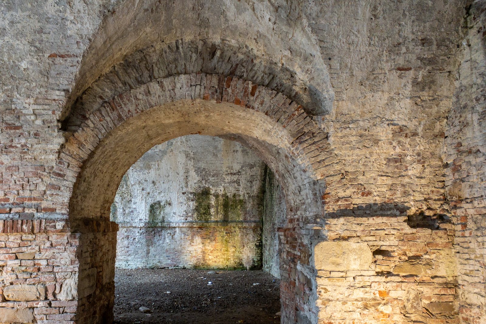 A thick stone archway in an old wall, its opening leading toward daylight.
